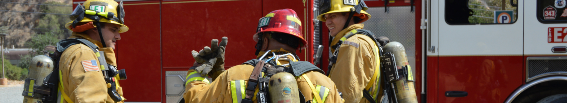 Three fire fighters talking in front of a red fire truck