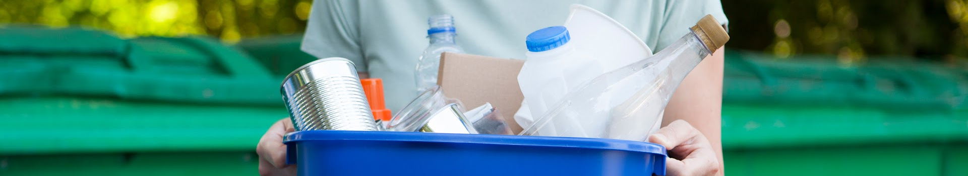 close up of person holding a blue recycling bin with empty bottles and cans in it